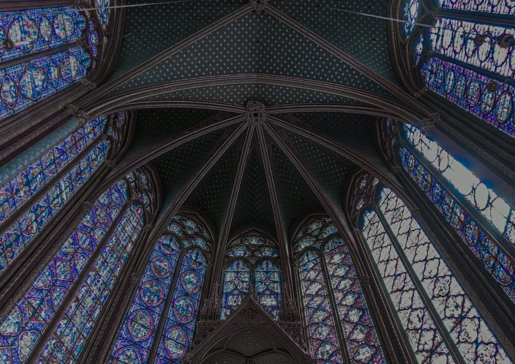 Photographie du plafond de la Sainte Chapelle. On voit les vitraux, très hauts, dans des tons bleus foncés et violets, ainsi que les arcs en marbre.