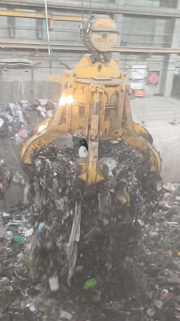 Image d'un grappin géant attrapant des tonnes de déchets dans une fosse. Pinpin se trouve dans le grappin.