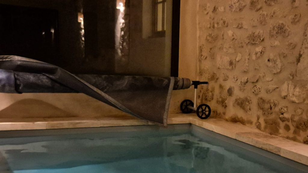 une petite piscine intérieure avec au fond une baie vitrée qui donne sur le noir de la nuit
