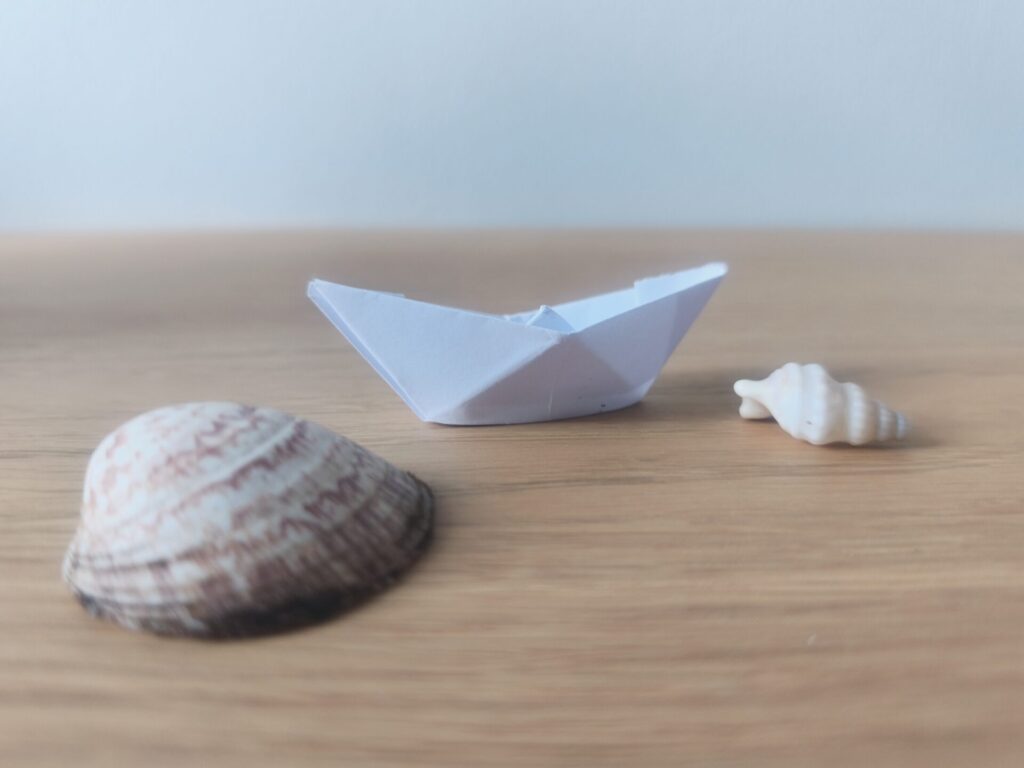 Origami de bateau et deux coquillages posés sur une table
