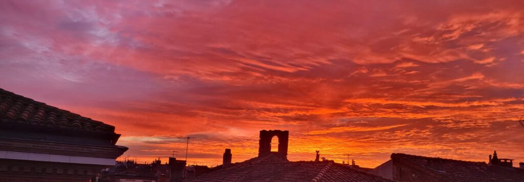 Photo d'un lever de soleil qui colore les nuages du jaune au rose profond avec vue sur des toits d'immeubles