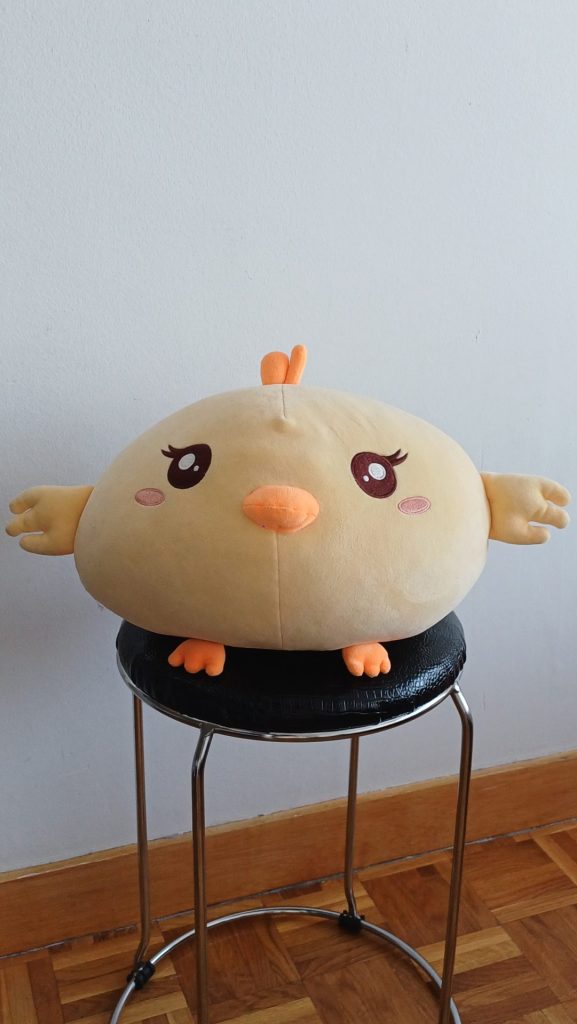 Photo d'un doudou d'un énorme poussin tout rond et tout doux, assis sur un tabouret.