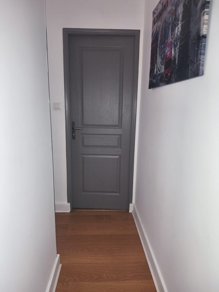 Couloir aux murs blancs avec une porte fermée grise.